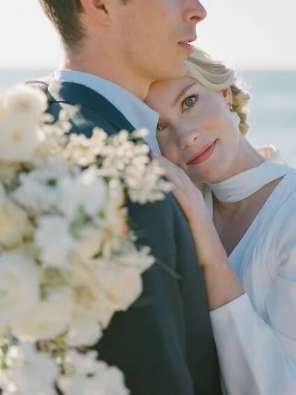 Romantic wedding portrait featuring a couple embracing with white flowers in soft light in Carmel-by-the-Sea.