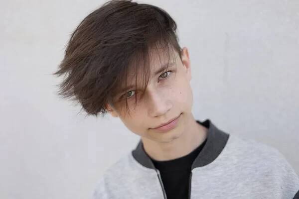Hezký mladý muž se stylovým účesem. Portrét dospívajícího chlapce s mladým účesem stojí na šedém pozadí a dívá se do kamery — Stock obrázek