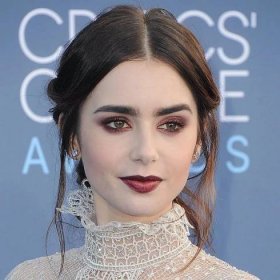 Lily Collins wears burgundy eyeshadow and lipstick and a messy updo