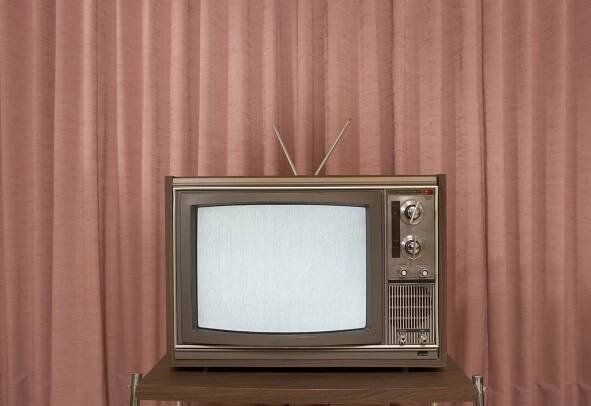 Old television on stand, in front of curtain