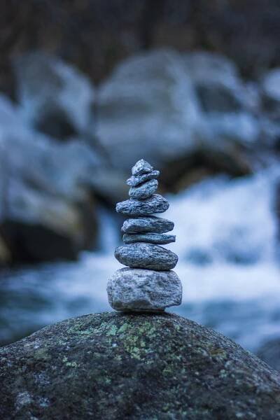 Free A vertical stack of stones balanced on a rock by a flowing river, showcasing nature's calm. Stock Photo