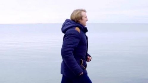 Mladý muž běží v krásné přírodní krajině u moře v kabátě