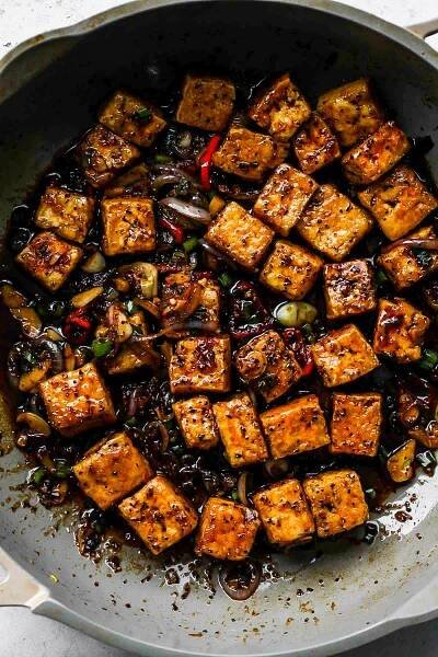 Cubes of tofu in a grey skillet after being tossed in black pepper sauce.