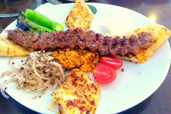 A long Adana kebab served on flatbreads with a side of onion and green peppers.