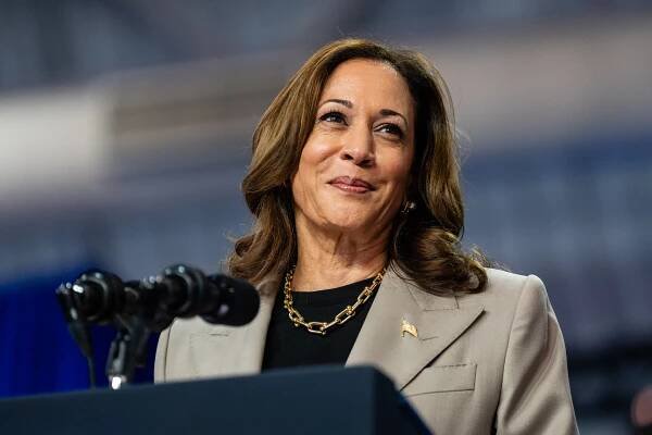 Kamala Harris smiles while standing at a lectern with a microphone.
