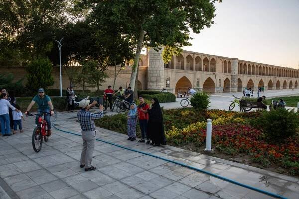 People pose for photos in front of a bridge with arches and turrets.