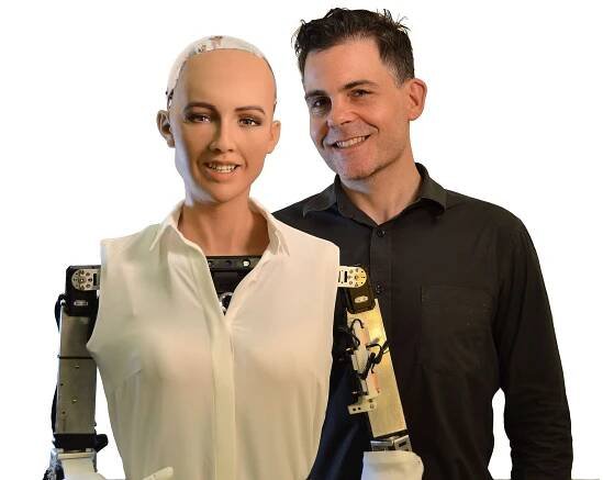 David Hanson, a smiling dark haired man, poses with Sophia, a realistic female humanoid robot whose skin and face mimic a humans.