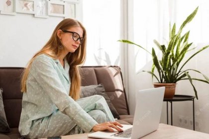 Side view of woman in pajamas working on laptop at home