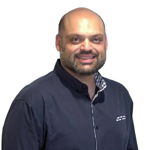 Smiling man with a beard wearing a dark button-up shirt, standing against a plain white background.
