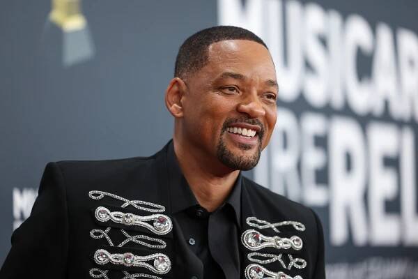 Will Smith smiling, wearing a black jacket with decorative embellishments, at the 2025 Grammys.