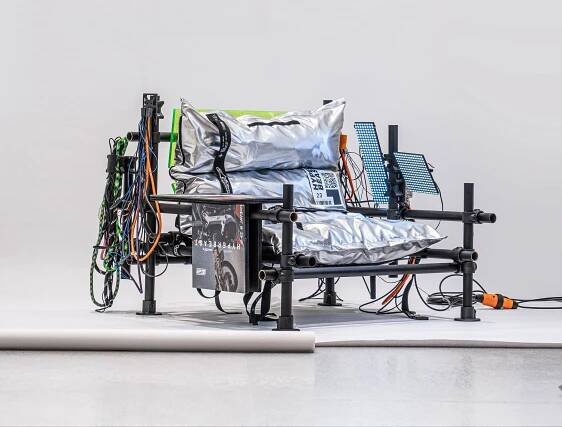 A modern, industrial-style chair with metallic cushions and colorful cables, showcasing an innovative design in a minimalist setting.