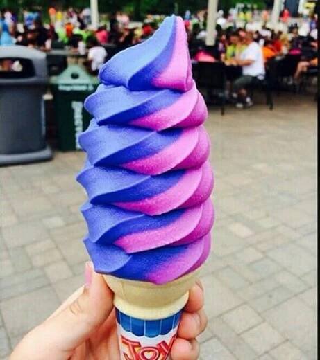 a hand holding an ice cream cone with purple and blue swirled topping