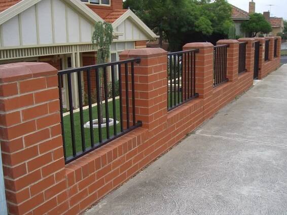 a red brick fence with black iron bars on the top and bottom, in front of a house