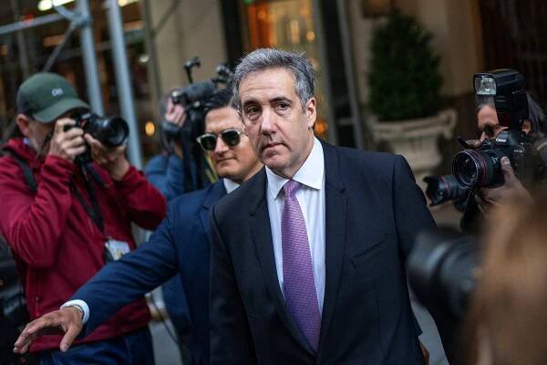 Michael D. Cohen leaves his apartment in a dark suit and purple ties as photographers take his picture.