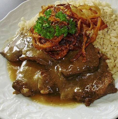 a white plate topped with meat covered in gravy and onions next to rice