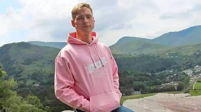 Man in pink hoodie in mountainous landscape.