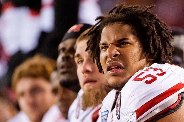 Football player in white jersey with red text shown on sidelines with intense expression during game.