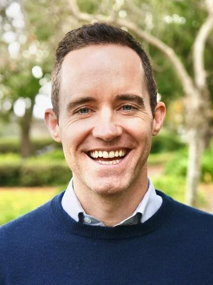 Patrick O'Donnell smiling in dark blue sweater with green trees in background