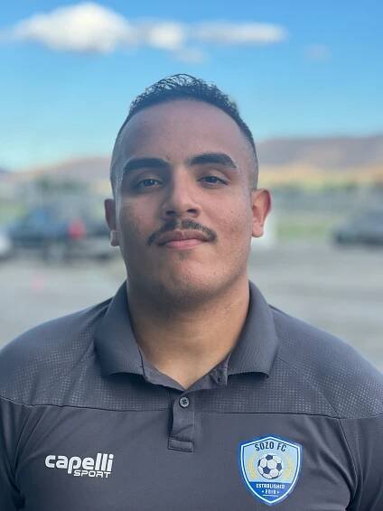A man with a mustache is wearing a black polo shirt.