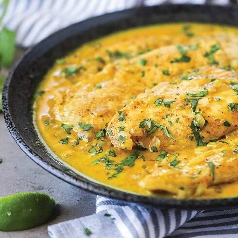 Curry sauce with coconut milk smothered over chicken breast meat is shown plated in a black dish.