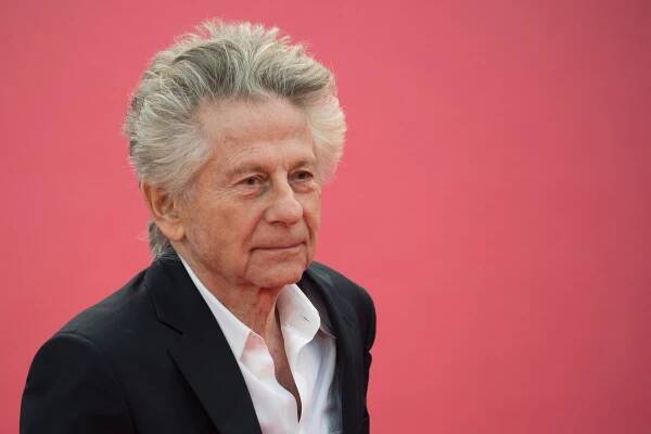 Roman Polanski in front of a pink backdrop.