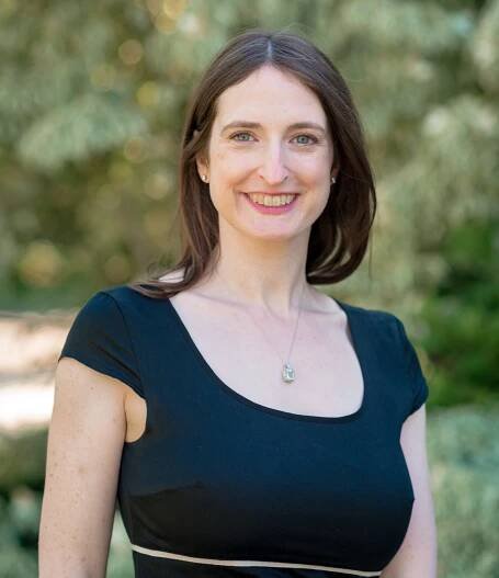 White woman with dark brown hair, wearing black top, blue-green eyes.