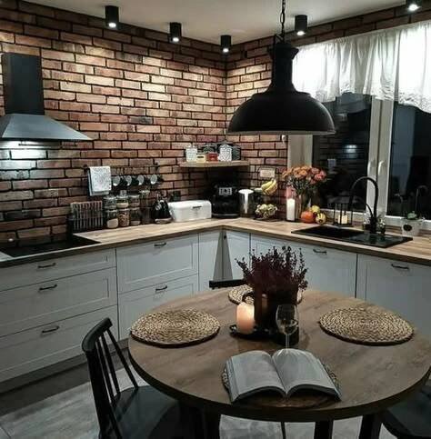 an open book is sitting on a table in the middle of a kitchen with brick walls