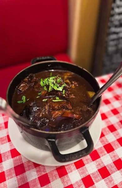 boeuf bourguignon in a cast iron pot on a white plate against a red checkered table cloth at Chez Fernand Paris