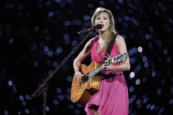 Taylor Swift in a pink dress, playing a guitar and singing into a microphone during 'The Eras Tour' at Olympiastadion in Munich, Germany on July 27, 2024