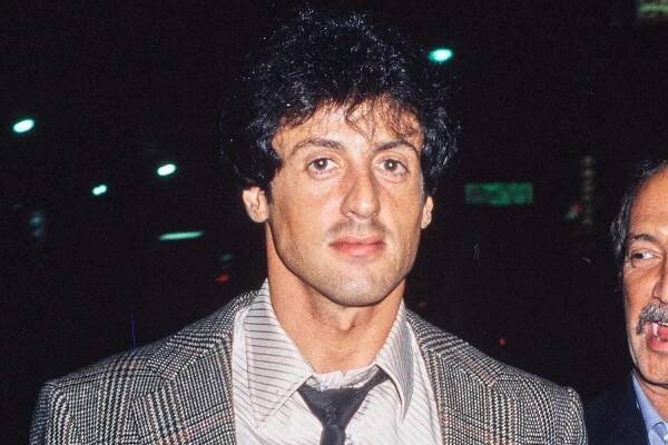 American actor Sylvester Stallone, wearing a tweed blazer over a white striped shirt black patterned tie, and jeans, United States, circa 1977.