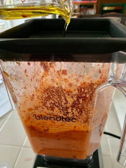 Streaming olive oil into the red pepper sauce running in the high speed blender