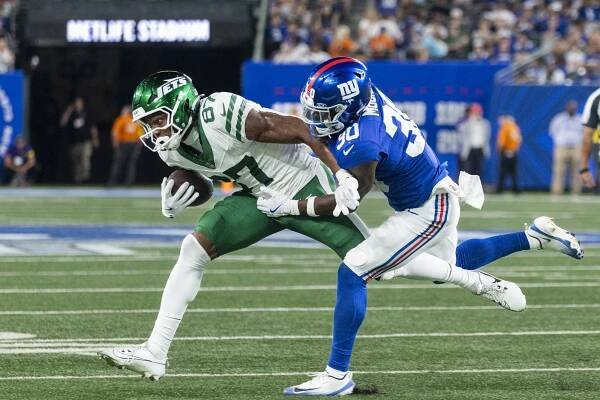 New York Jets player carrying the ball, being tackled by a New York Giants player.