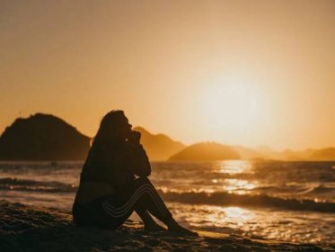 silhouette of woman sitting on beach during sunset