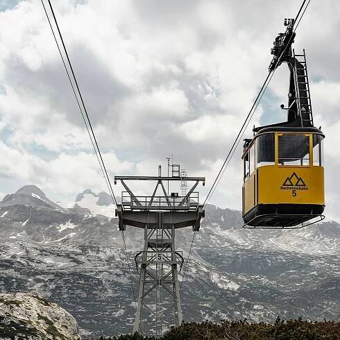 Seilbahn mit gelber Gondel und Nummer 5 vor einem Bergpanorama mit Wolkenhimmel.