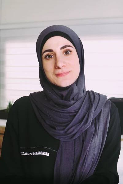 A headshot of Sara wearing a purple hijab.
