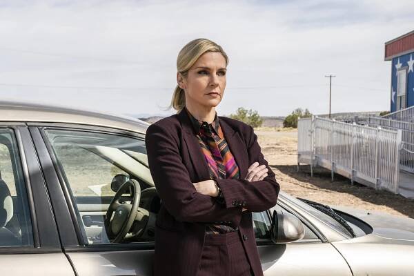 A woman (Rhea Seehorn as Kim Wexler on "Better Call Saul") leaning against a silver car with her arms crossed..