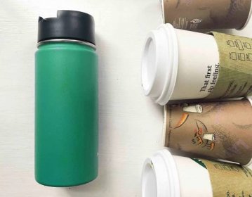 one green reusable travel mug next to four disposable coffee cups