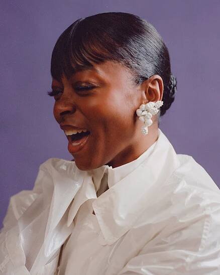 A close-up of a woman in a white shirt with large white earrings. 