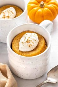 Pumpkin mug cake with whipped cream and a sprinkle of spice on top.