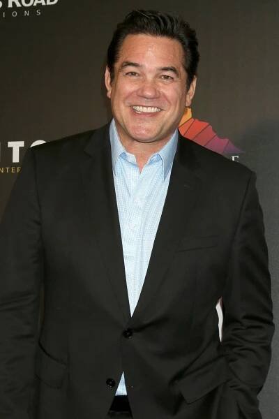 Dean Cain posing and smiling an a black jacket and blue button-down shirt. 