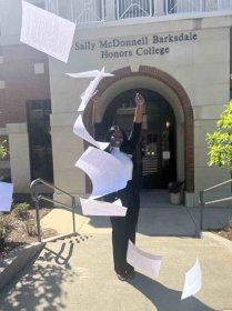 Moore wears a back sweater and pants as she throws the papers of her dissertation in the air in celebration of her completion. 