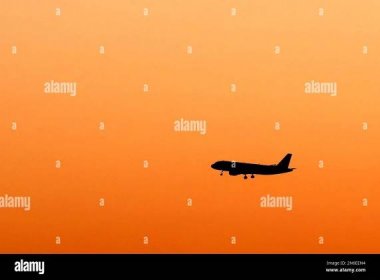 Airplane silhouetted flying at early dawning. Stock Photo