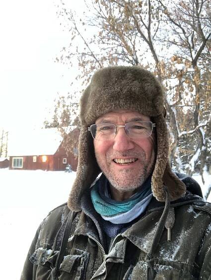 Head and shoulders of a smiling man in a fuzzy hat outside in winter.