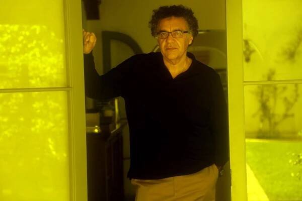 Rodrigo Garcia, looking serious, stands between a set of glass doors that reflect yellow light