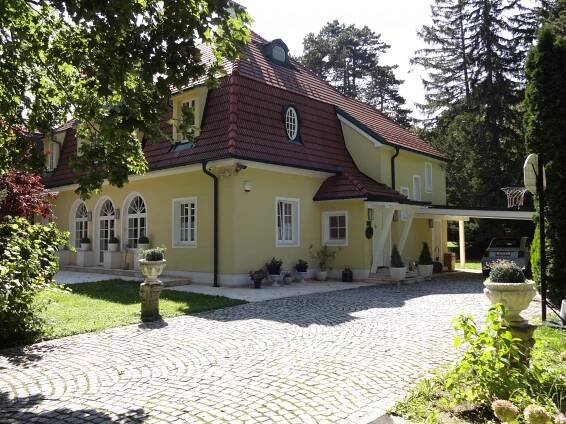 große schöne Villa in Maria Enzersdorf, gelbe Fassade, weiße Fenster, rotem ausgebautem Dach, gepflasterte Einfahrt, grüne Umgebung