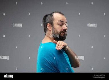 Bearded man in blue t-shirt showing contemptuous gesture with a hand over his shoulder, as if dusting off, and grimace of disgust on his face. Side po Stock Photo