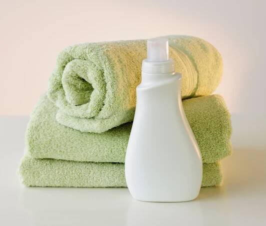 Rolled and folded towels with a bottle of detergent on a white surface