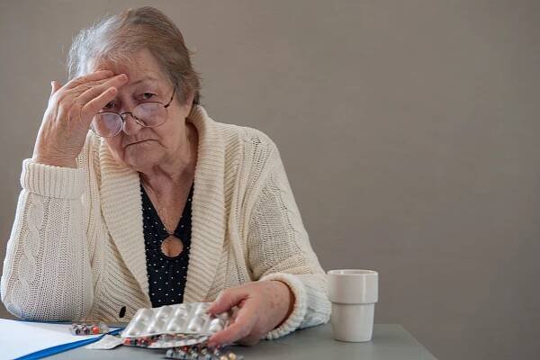 Elderly woman resembling Miriam A. Ferguson, with a beautiful wrinkled face, holding pills in her hands to select medicines