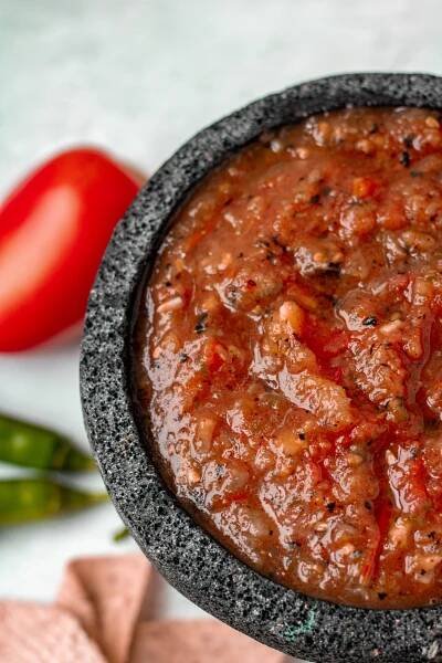 Close up of salsa roja in stone molcajete. Tomato and serrano pepper props