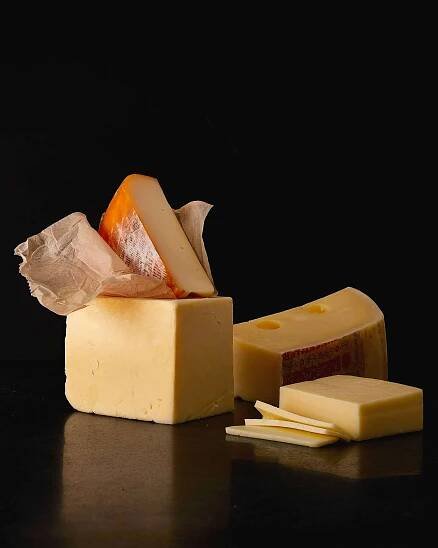 pieces of semi hard cheese, including cheddar and Emmental, on black surface